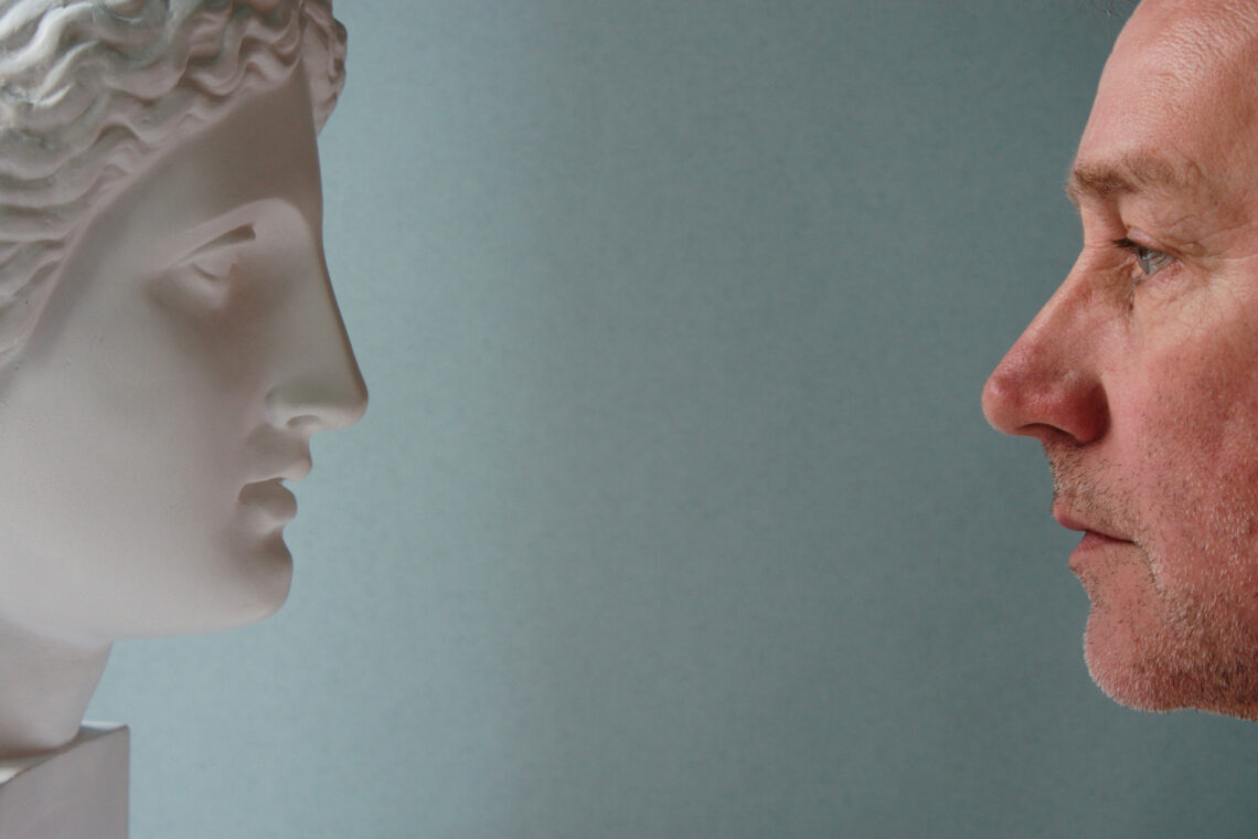 Due volti di profilo, a sinistra quello di una statua di donna, a destra quello di un uomo