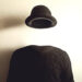 Fotografia che ritrae un maglione nero e un cappello nero che fluttua nell'aria sopra lo stesso, davanti a un muro bianco su cui si proiettano le ombre del maglione e del cappello. Sembra di osservare un uomo invisibile.