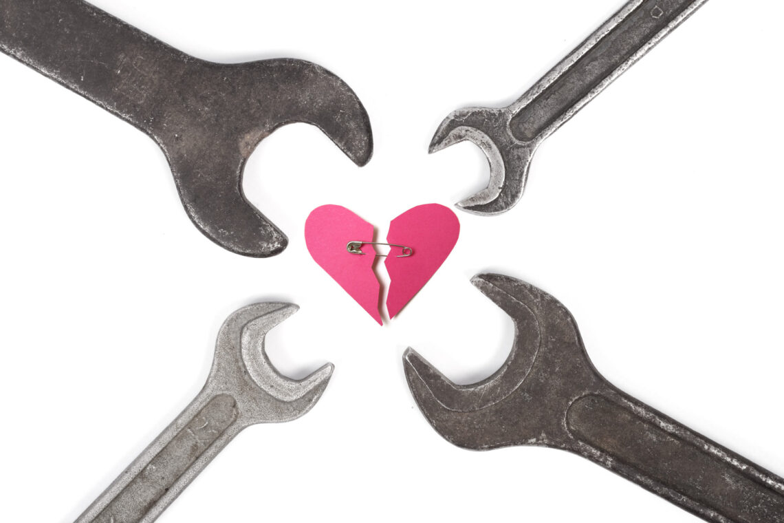 Una fotografia che ritrae, al centro, un cuore stilizzato, rosa, spezzato; le due parti sono tenute vicine da una spilla da balia; disposte intorno al cuore, con la parte che abitualmente si usa per girare i bulloni vicina allo stesso, ci sono quattro chiavi inglesi di diverse misure.