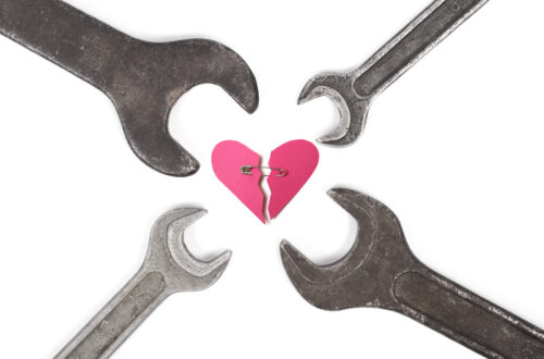 Una fotografia che ritrae, al centro, un cuore stilizzato, rosa, spezzato; le due parti sono tenute vicine da una spilla da balia; disposte intorno al cuore, con la parte che abitualmente si usa per girare i bulloni vicina allo stesso, ci sono quattro chiavi inglesi di diverse misure.