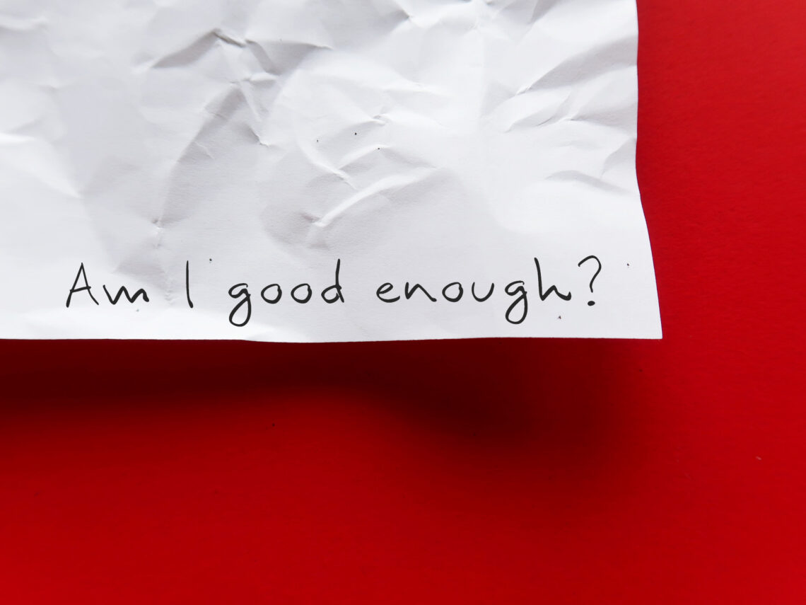 Fotografia che ritrae l'angolo inferiore destro di un foglio di carta stazzonata appeso a un muro russo. Sul foglio qualcuno ha scritto a mano con un tratto nero "Am I good enough?"