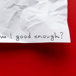 Fotografia che ritrae l'angolo inferiore destro di un foglio di carta stazzonata appeso a un muro russo. Sul foglio qualcuno ha scritto a mano con un tratto nero "Am I good enough?"