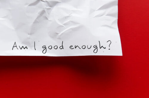 Fotografia che ritrae l'angolo inferiore destro di un foglio di carta stazzonata appeso a un muro russo. Sul foglio qualcuno ha scritto a mano con un tratto nero "Am I good enough?"