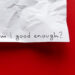 Fotografia che ritrae l'angolo inferiore destro di un foglio di carta stazzonata appeso a un muro russo. Sul foglio qualcuno ha scritto a mano con un tratto nero "Am I good enough?"