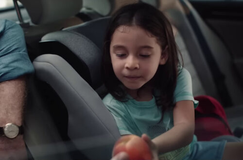Un fotogramma da una pubblicità dell'Esselunga: una bambina seduta nella poltroncina di sicurezza sul retro di un'automobile porge una pesca a suo padre, accucciato fuori dallo sportello aperto al suo fianco.