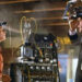 Un fotogramma dal film “Ritorno al futuro” in cui si vede, sullo sfondo, un laboratorio con un macchinario pieno di interruttori, lucette e cavi che ne fuoriescono in una nebbiolina fumosa, in primo piano e di profilo ci sono Marty, il protagonista, sulla sinistra, e Doc, il coprotagonista, sulla destra, uno di fronte all’altro. Marty, con una ventosa appiccicata sulla fronte, dalla quale escono dei cavi sottili che vanno al macchinario, guarda con aria sbalordita e un po’ inebetita Doc, il quale a sua volta lo fissa con aria spiritata reggendo con entrambe le mani una sorta di ampio casco pieno di lucette che ha in testa, a sua volta collegato alla macchina sullo sfondo.