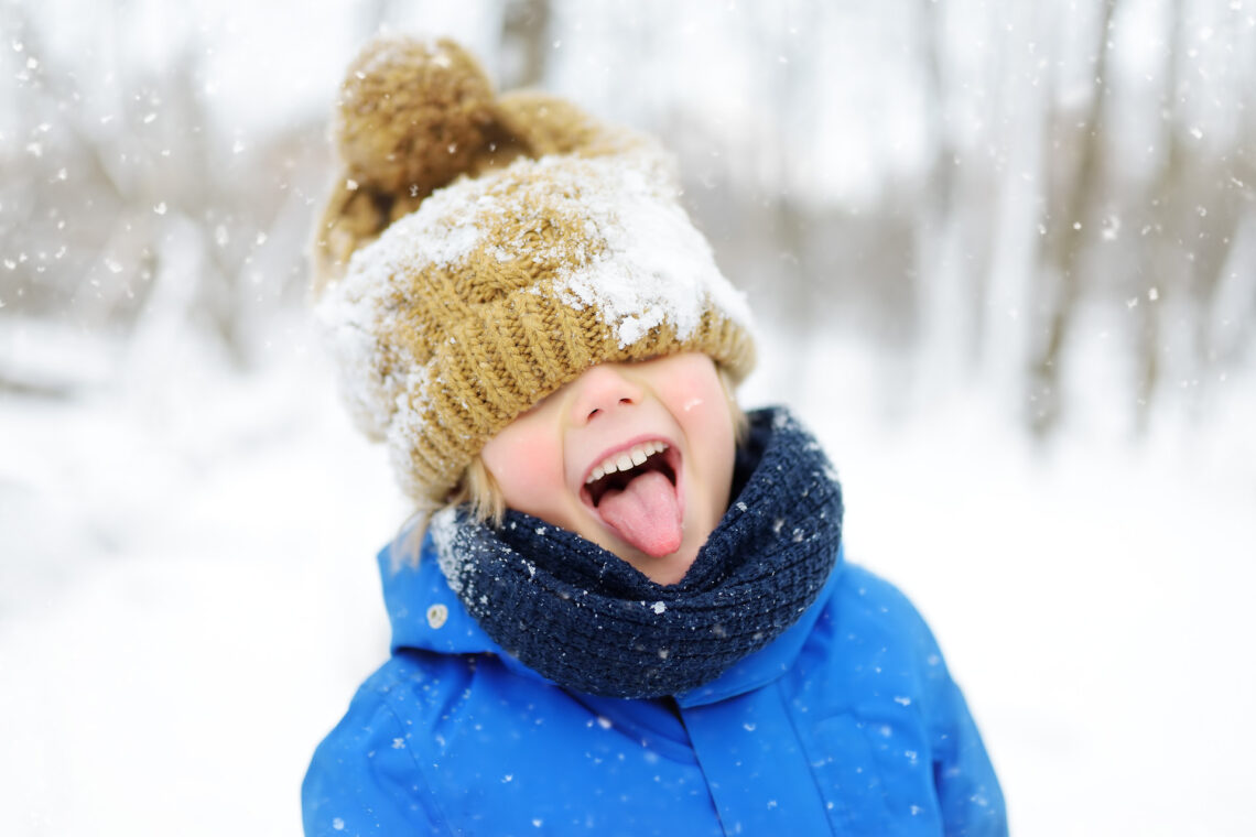 Una foto che ritrae, davanti a uno sfondo innevato con un boschetto di alberi spogli dalla corteccia chiara in fondo, un bambino in giacca imbottita azzurra da sci, con un bavero alto a coprirne il collo, un berrettone di lana beige sulla testa calato fin sopra gli occhi, che fa la linguaccia sorridendo verso l’obiettivo.