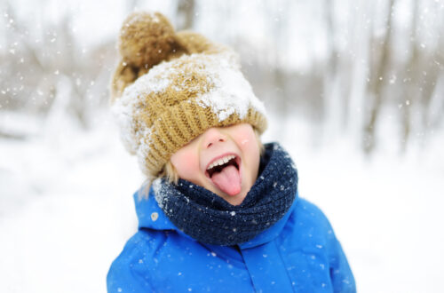 Una foto che ritrae, davanti a uno sfondo innevato con un boschetto di alberi spogli dalla corteccia chiara in fondo, un bambino in giacca imbottita azzurra da sci, con un bavero alto a coprirne il collo, un berrettone di lana beige sulla testa calato fin sopra gli occhi, che fa la linguaccia sorridendo verso l’obiettivo.
