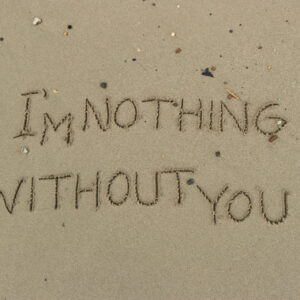 Una fotografia che ritrae da vicino il bagnasciuga di una spiaggia di sabbia con piccole conchiglie, rametti e sassolini. Al centro c'è una scritta tracciata nella sabbia con un dito, "I'm nothing without you" ("Senza te sono niente"), e destinata a essere cancellata dalla prossima onda abbastanza lunga.