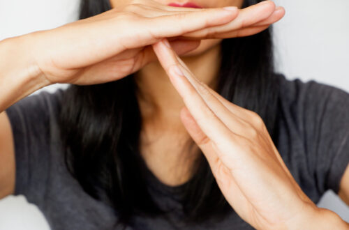 Una foto che ritrae una donna con il volto coperto dalle mani che tiene nella posizione con cui si chiede, negli sport soprattutto, una pausa: la destra in orizzontale sopra la sinistra in verticale, che appoggia le falangi al centro del palmo della destra.