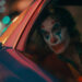 Un fotogramma dal film “Joker” del 2019, di Todd Phillips, con Joaquin Phoenix nella parte del protagonista, Arthur Fleck / Joker, mentre guarda fuori dal finestrino dal sedile posteriore, a destra, di un’auto della polizia, truccato da pagliaccio e con un’aria meditabonda.