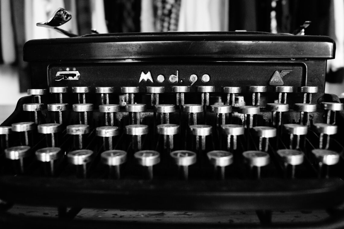 Fotografia che ritrae una macchina per scrivere meccanica, di colore nero, con tanti tasti metallici disposti su quattro file, una sopra l'altra, che perciò somigliano a seggiolini di uno spalto di un teatro o di un centro sportivo.