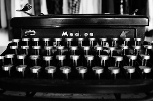 Fotografia che ritrae una macchina per scrivere meccanica, di colore nero, con tanti tasti metallici disposti su quattro file, una sopra l'altra, che perciò somigliano a seggiolini di uno spalto di un teatro o di un centro sportivo.
