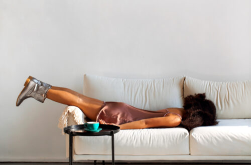 Una fotografia a colori, in formato 4:3, che ritrae una donna di colore, dal corpo asciutto e dalla testa coperta di folti capelli ricci, stesa di faccia su un divano bianco, con le braccia lungo i fianchi e la parte inferiore delle gambe che sporge oltre il poggiagomiti sinistro del divano stesso, in una posizione che dà l'idea di una grande stanchezza.