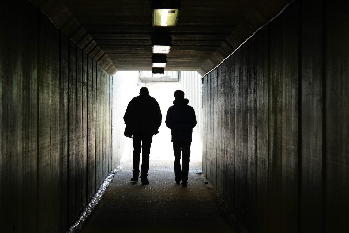 Una foto a colori, in formato orizzontale, che ritrae due persone che camminano verso la fine di un tunnel.