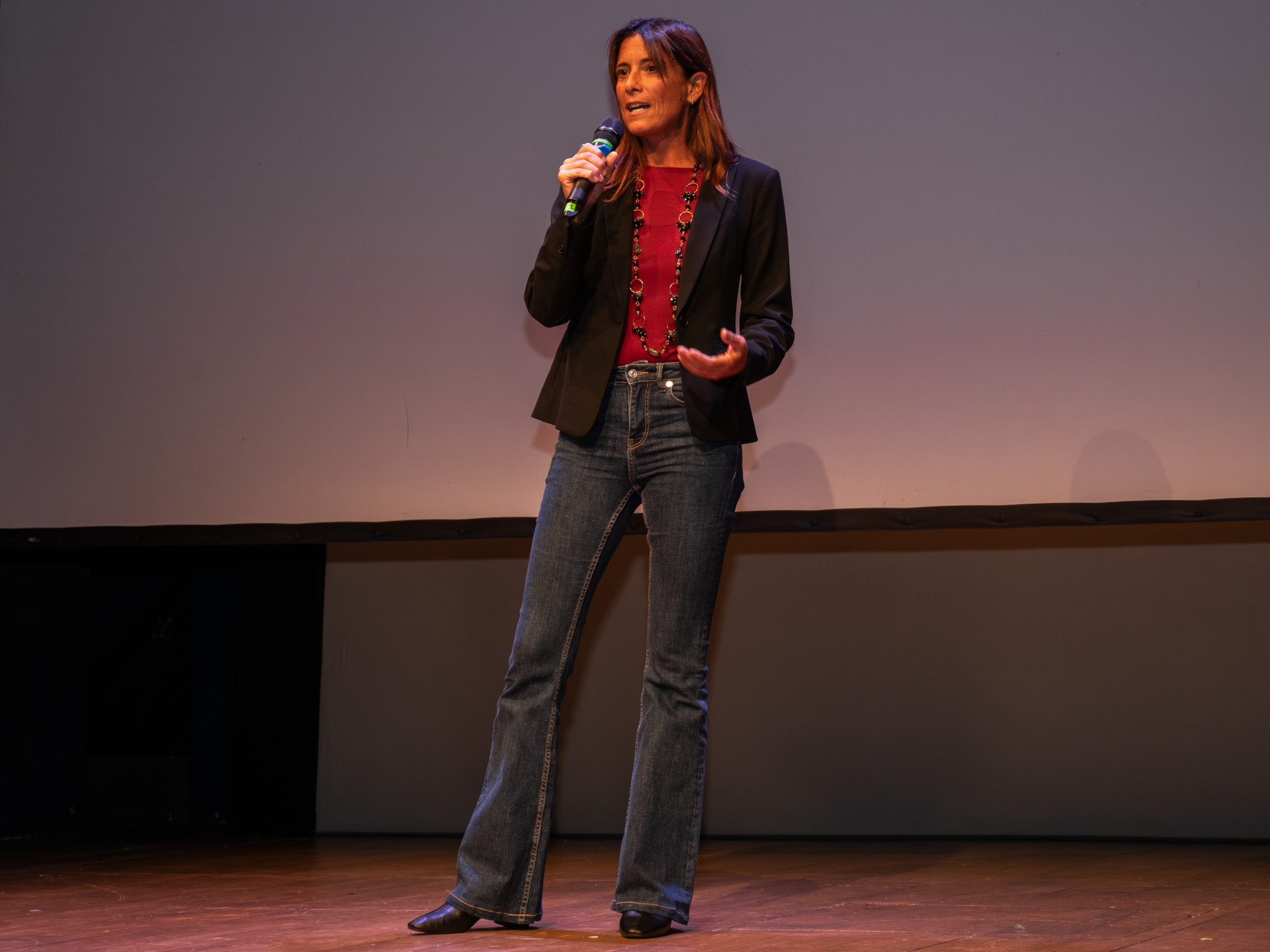 Una foto a colori, in formato orizzontale (4:3), che ritrae un palco sopra il quale si trova una donna in piedi che parla in un microfono.