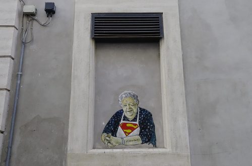 Su un'asse che chiude una finestra incastonata in un muro di cemento grigio e contornata da una specie di cornice di cemento più chiaro c'è un murale che ritrae la sora Lella (l'attrice Elena Fabrizi) come fosse seduta alla finestra, con le braccia appoggiate sul davanzale, mentre sorridendo fa l'occhiolino con l'occhio sinistro. Hai i capelli bianchi, indossa una veste blu a motivi bianchi e, sopra quella, un grembiule bianco con il simbolo di Superman sul petto.