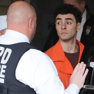 Una foto che ritrae Luigi Mangione mentre viene caricato su una macchina da alcuni agenti della polizia di New York.