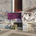 Una foto a colori, in formato orizzontale (4:3), che ritrae un muro d'angolo della parte inferiore - dal suolo fino al primo piano - di una casa. Sul muro c'è una scritta, "Ramy per sempre nei nostri cuori"; ce n'è un'altra, "Verità per Ramy", su uno striscione bianco appeso a sinistra a un fermaglio all'angolo inferiore destro di una finestra chiusa, e a destra a un palo segnaletico. Sul davanzale della finestra ci sono inoltre sei ceri rossi. In basso, sul marciapiedi, ci sono fiori singoli (due rose rosse), due vasetti e un mazzo di fiori vari. Davanti alle rose, sull'asfalto, ci sono tante candeline bianche, spente.