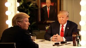 Una foto a colori, in formato orizzontale, che ritrae Donald Trump davanti a uno specchio da camerino. Dello specchio però c'è solo la cornice, e l'uomo dall'altra parte è un intervistatore acconciato e truccato per somigliargli. E' una foto di scena di un'intervista a Trump andata realmente in onda.