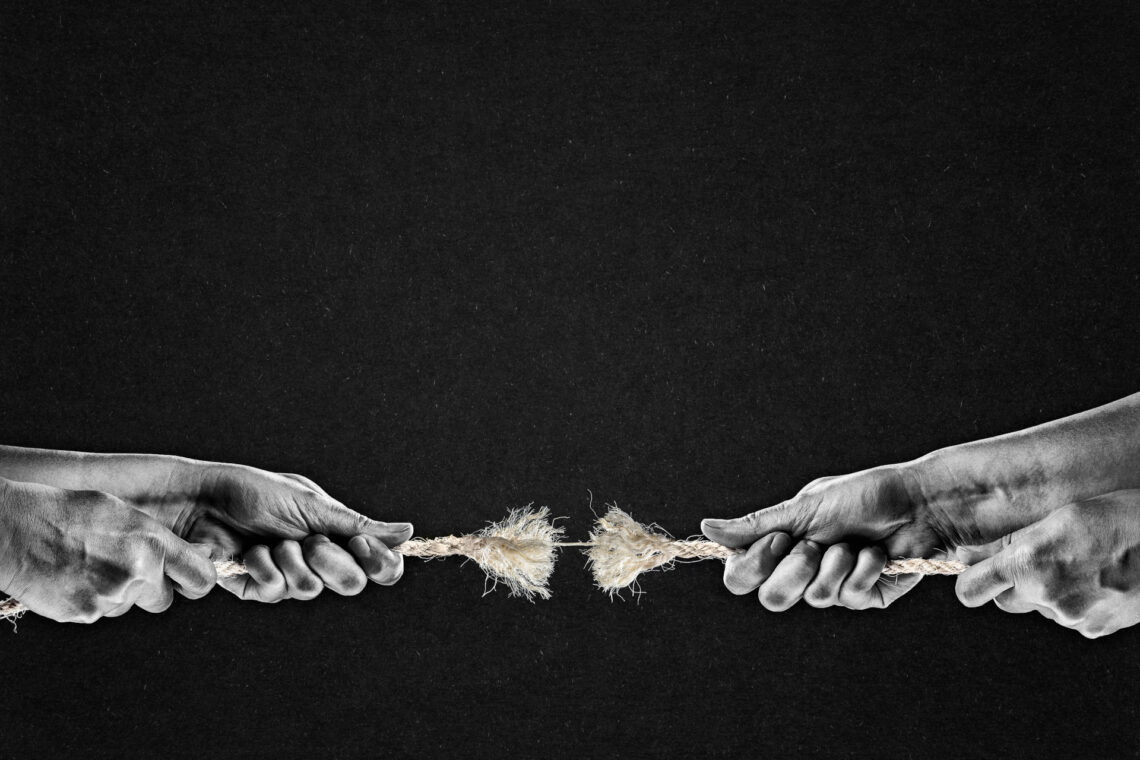 Una foto in bianco e nero, in formato orizzontale, che ritrae, davanti a uno sfondo grigio scurissimo e granuloso, le mani di due uomini che stanno facendo il tiro alla fune; la fune, al centro, è tutta sfilacciata, e sta per spezzarsi: ne resta solo una fibra sottile.