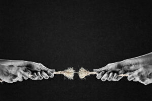 Una foto in bianco e nero, in formato orizzontale, che ritrae, davanti a uno sfondo grigio scurissimo e granuloso, le mani di due uomini che stanno facendo il tiro alla fune; la fune, al centro, è tutta sfilacciata, e sta per spezzarsi: ne resta solo una fibra sottile.