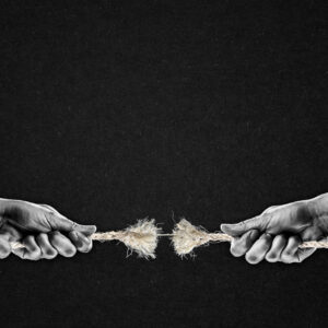 Una foto in bianco e nero, in formato orizzontale, che ritrae, davanti a uno sfondo grigio scurissimo e granuloso, le mani di due uomini che stanno facendo il tiro alla fune; la fune, al centro, è tutta sfilacciata, e sta per spezzarsi: ne resta solo una fibra sottile.