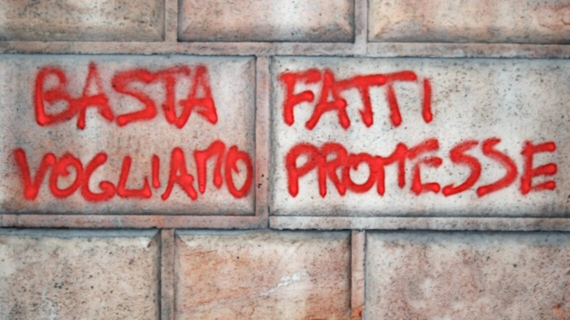 Una foto a colori, orizzontale, che ritrae un muro con una scritta a spray rosso: "Basta fatti vogliamo promesse".