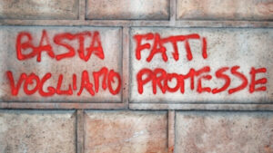 Una foto a colori, orizzontale, che ritrae un muro con una scritta a spray rosso: "Basta fatti vogliamo promesse".