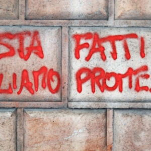 Una foto a colori, orizzontale, che ritrae un muro con una scritta a spray rosso: "Basta fatti vogliamo promesse".
