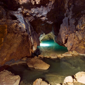 Una foto a colori, in formato orizzontale, che ritrae alcuni piccoli laghetti d'acqua trasparente, di colore verde-azzurro, in una caverna parizlalmente illuminata dall'alto dalla luce del sole che entra attraverso dei buchi sul suo soffitto.