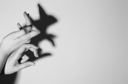 Una foto in bianco e nero che ritrae un muro su cui due mani di donna sovrapposte l’una all’altra, che spuntano dal bordo sinistro con le dita in una posizione molto particolare, proiettano un’ombra che appare come il profilo di un coniglio in piedi sulle zampe posteriori, con le zampe anteriori che sporgono in avanti e un paio di lunghe orecchie sopra la testolina.