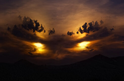 Una foto a colori che ritrae un tramonto. La luce e la disposizione delle nubi sembrano dar forma a due occhi cattivi nel cielo.