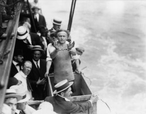 Una foto in bianco e nero, in formato orizzontale, che ritrae Harry Houdini, il celebre illusionista ed escapologo, attorniato da tanti passeggeri di una nave, mentre protende le mani coi polsi legati tra loro da un paio di manette, in piedi all'interno di una cassa aperta che sta per essere chiusa e gettata in mare.