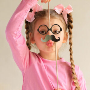 Una foto che ritrae al centro una bambina vestita di rosa e con lunghe trecce che le scendono ai lati del volto mentre per gioco finge di essere un uomo con un paio di occhiali neri rotondi e un paio di baffi altrettanto neri e posticci, sotto i quali manda un bacino verso l'obiettivo.