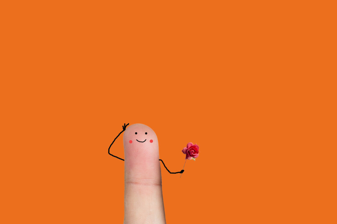 Una foto che ritrae al centro l’estremità di un dito umano, un indice, teso verso l’alto davanti a uno sfondo arancione. Sulla falange del dito sono disegnati, con tratto molto infantile, un paio di occhi, una bocca sorridente e due gote rosse ai suoi lati. Poco al di sotto di questo viso, dai lati del dito escono due braccia: la sinistra porta la mano al lato sinistro della “testa”, con un gesto che appare un po’ vezzoso; la destra regge davanti al “busto” una rosa di colore rosa. Nell’insieme il dito sembra prepararsi a un incontro galante.