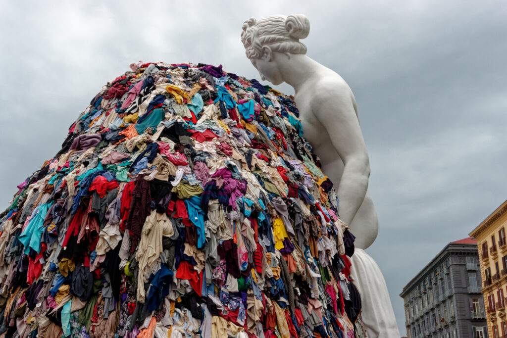 Napoli, Italia - 30 settembre 2023: La monumentale installazione artistica “Venere degli stracci” dell’artista contemporaneo Michelangelo Pistoletto è esposta all’aperto in città. Una classica scultura bianca raffigurante la dea romana si affaccia su un’enorme pila di indumenti colorati scartati. Questo iconico capolavoro dell’Arte Povera contrappone visivamente l’antica bellezza classica al consumismo e agli sprechi della moda fast fashion moderna, offrendo una potente riflessione culturale e sociale ai turisti di tutto il mondo e agli amanti dell’arte.
