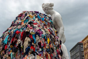 Napoli, Italia - 30 settembre 2023: La monumentale installazione artistica “Venere degli stracci” dell’artista contemporaneo Michelangelo Pistoletto è esposta all’aperto in città. Una classica scultura bianca raffigurante la dea romana si affaccia su un’enorme pila di indumenti colorati scartati. Questo iconico capolavoro dell’Arte Povera contrappone visivamente l’antica bellezza classica al consumismo e agli sprechi della moda fast fashion moderna, offrendo una potente riflessione culturale e sociale ai turisti di tutto il mondo e agli amanti dell’arte.